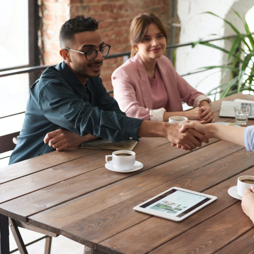 Deux jeunes professionnels assis à une table se serrent la main lors d'une séance de coaching individuel.