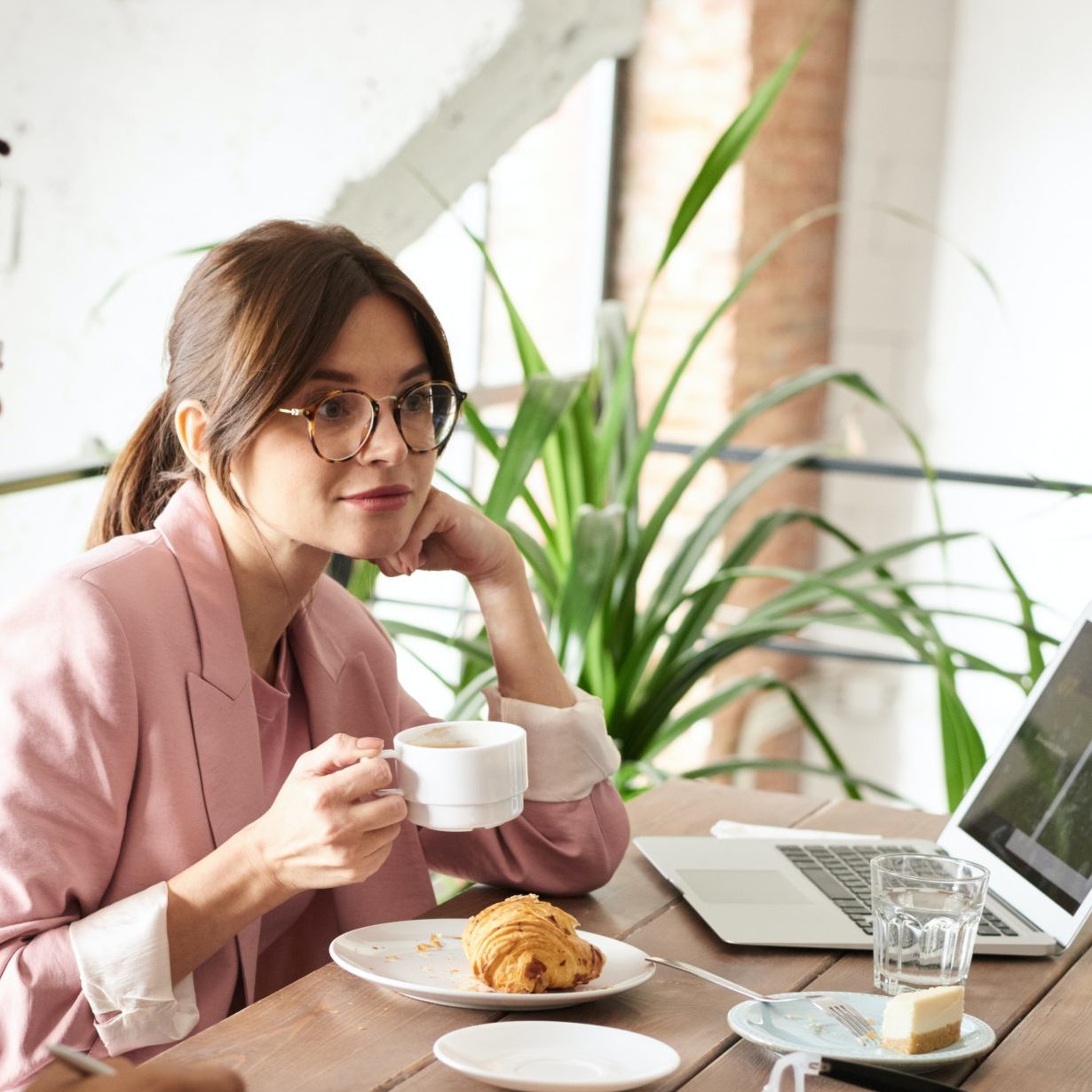 Bilan de compétence et congé parental sont compatible : cette image montre une jeune femme buvant un café et mangeant un croissant devant son ordinateur.